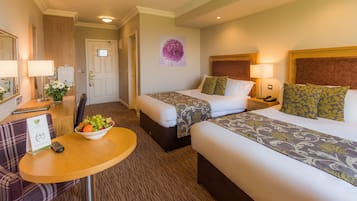 A hotel room with two beds, a desk with a bowl of fruit, a chair, and a wall-mounted picture.