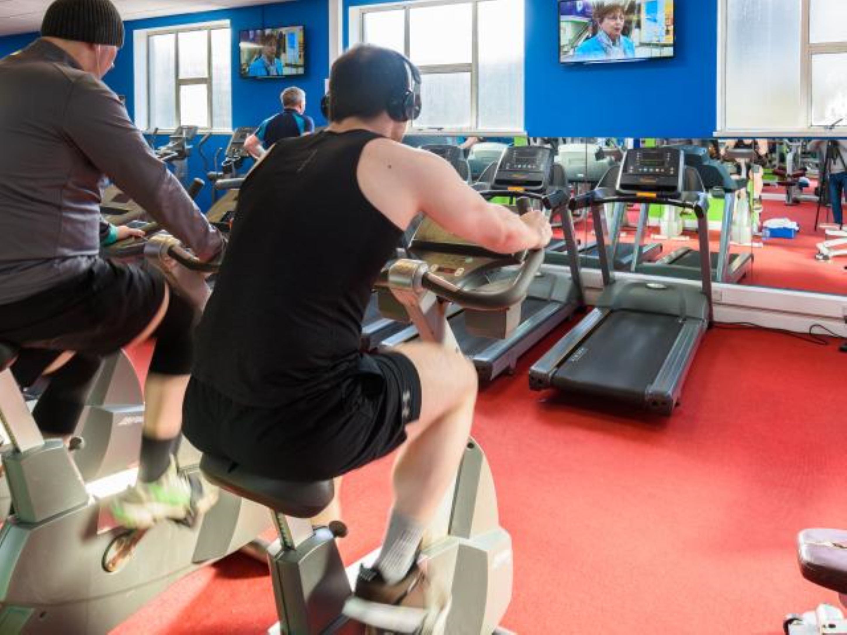 A gym with treadmills, stationary bikes, and a red carpet floor.