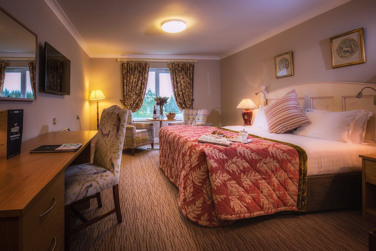 Une chambre d’hôtel avec un lit, un bureau, une chaise et une petite table avec une lampe.