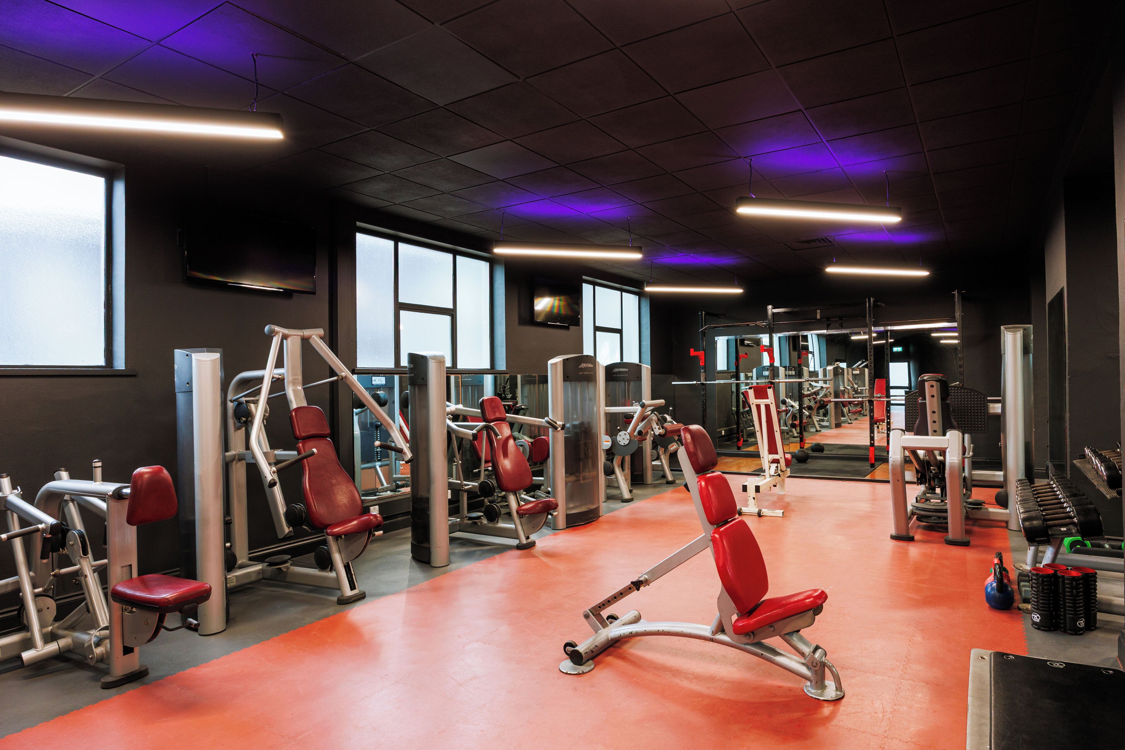 A gym with exercise machines, mirrors, and a red floor.