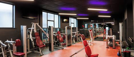 Un gimnasio con máquinas de ejercicio, espejos y suelo rojo.