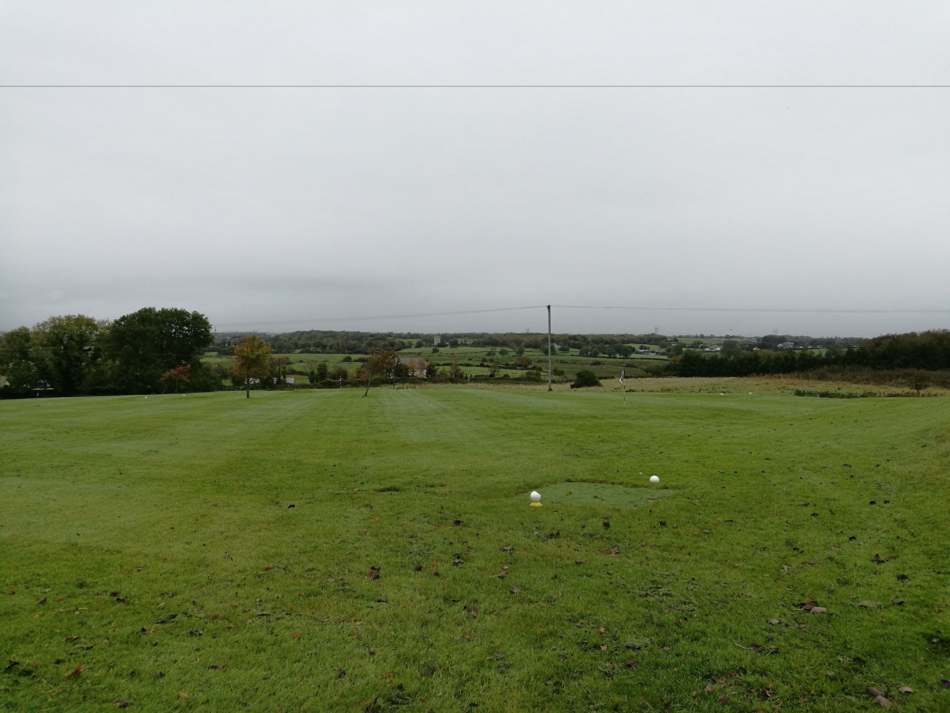 A golf course with a clear view of the landscape, including trees and distant buildings.