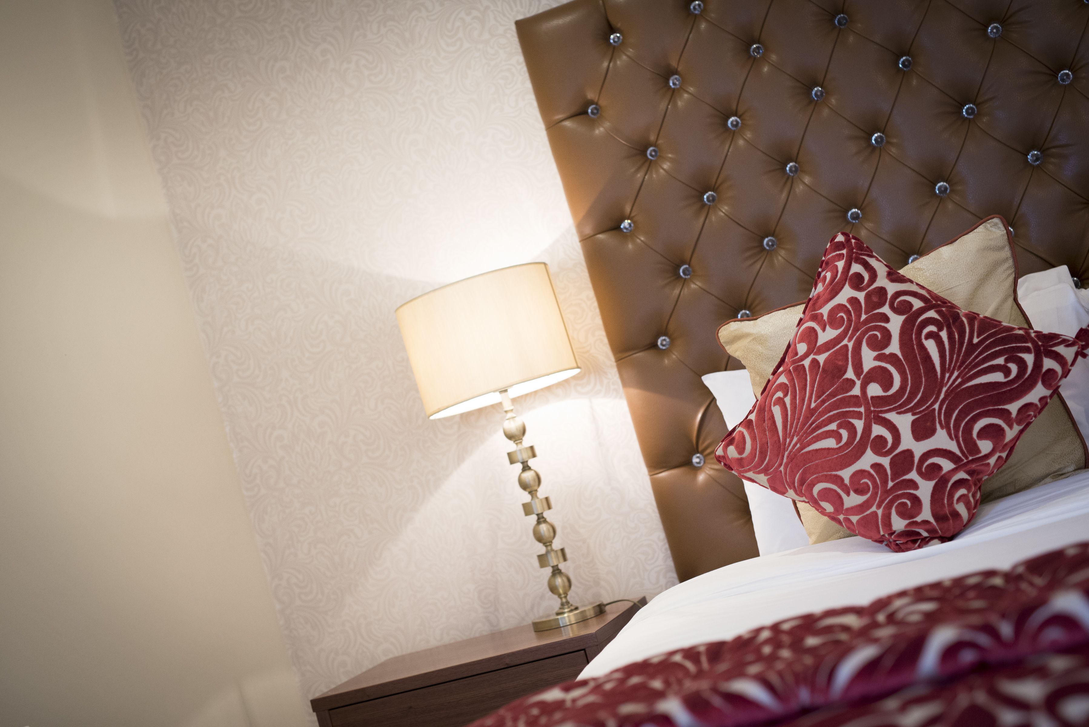A hotel room with a tufted headboard, a bedside lamp, and patterned bedding.