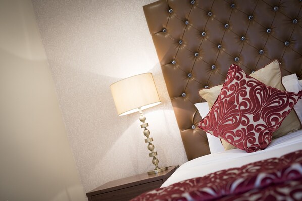 A hotel room with a tufted headboard, a bedside lamp, and patterned bedding.