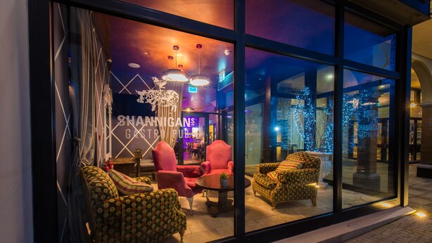 A hotel lobby with a glass facade, modern furniture, and a neon sign.