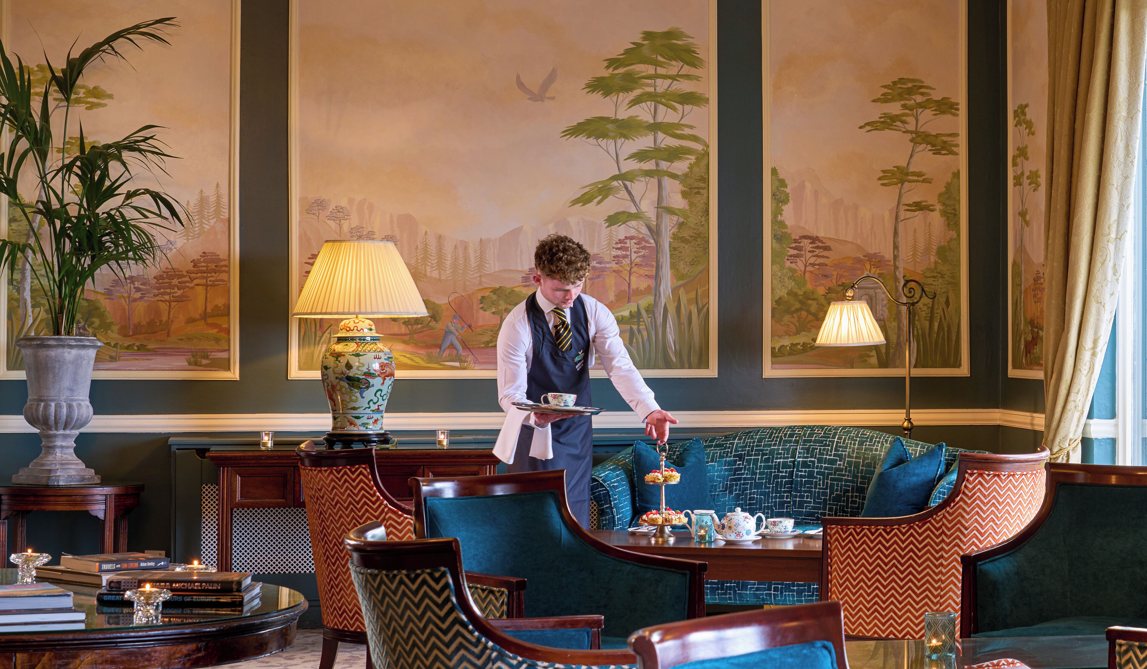 A well-appointed lounge area with a large painting, comfortable seating, and a service staff member attending to guests.