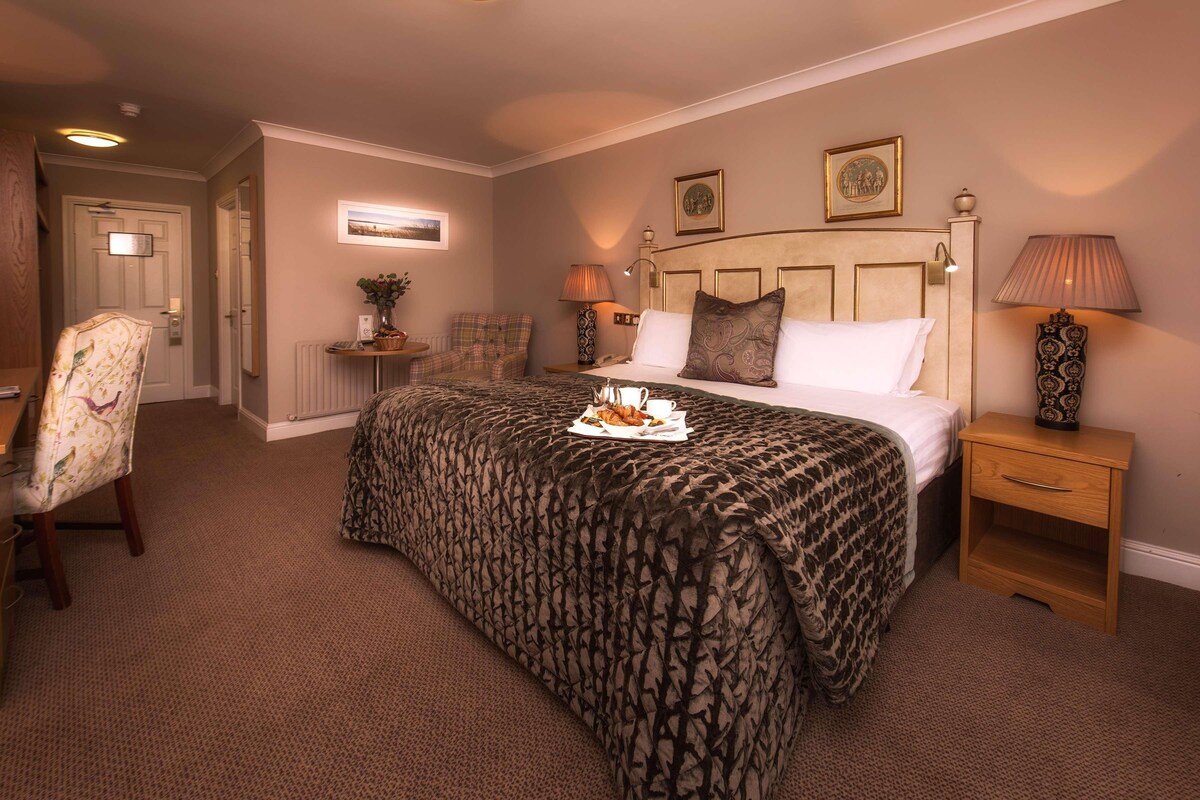 A hotel room with a bed, a nightstand, a chair, a lamp, and a picture on the wall.