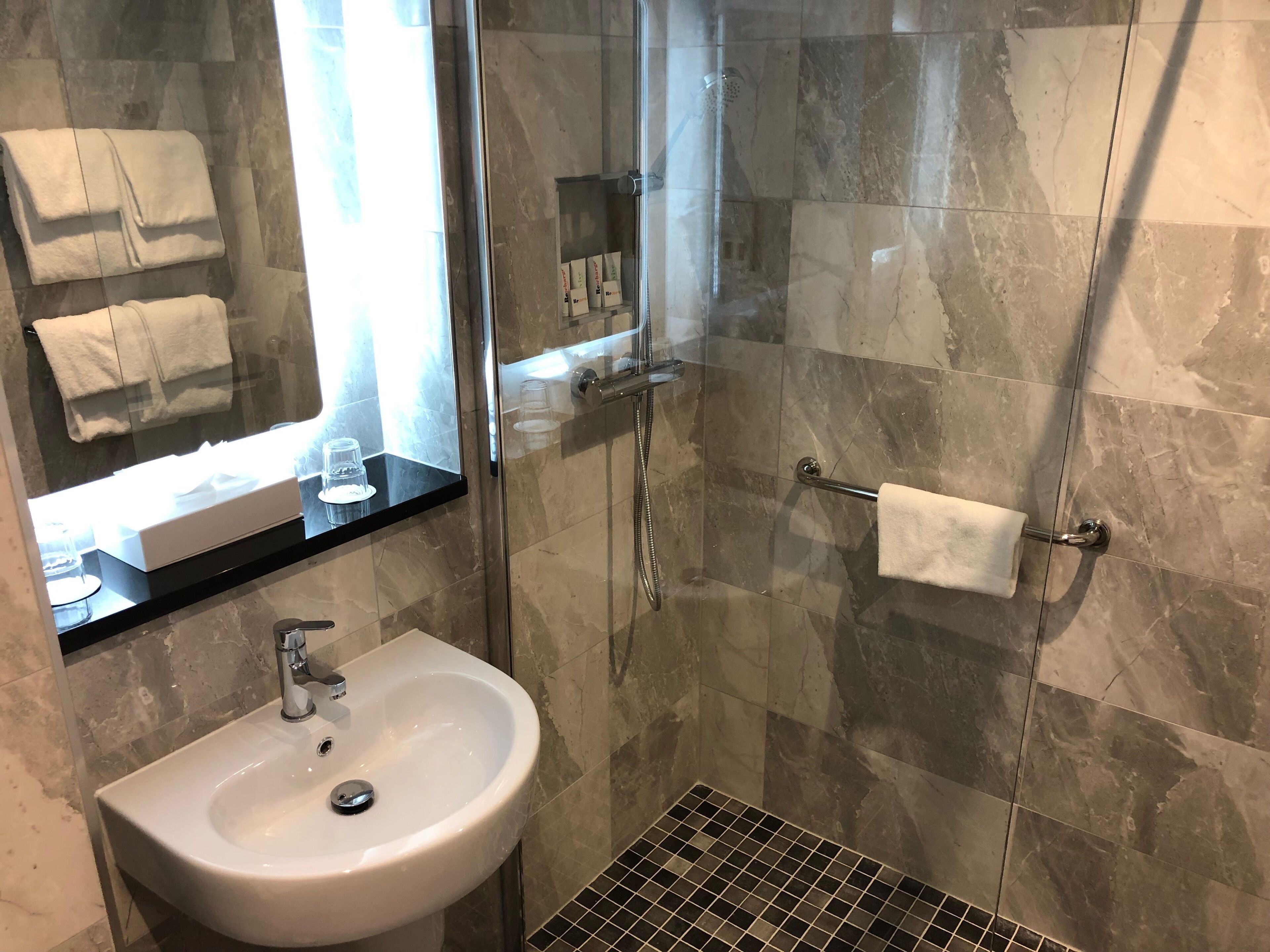 Une salle de bain avec une douche à parois de verre, un lavabo et un miroir.