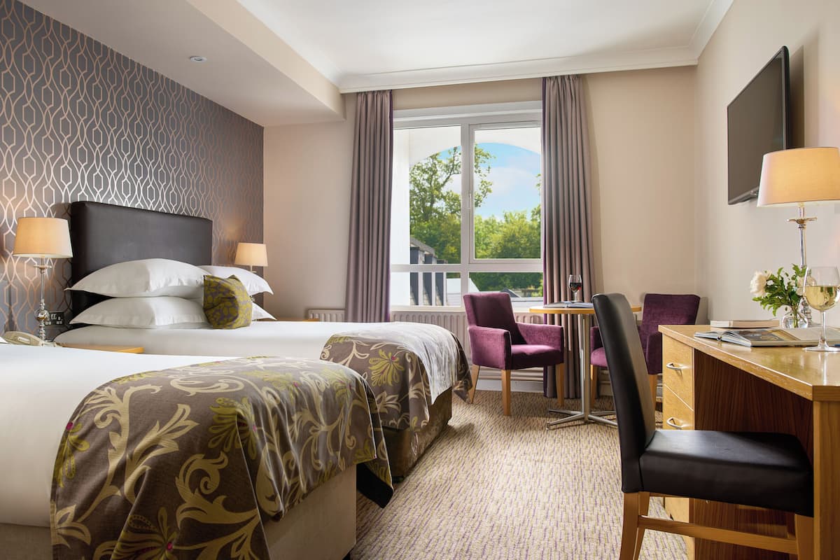A hotel room with two beds, a desk, and a chair.
