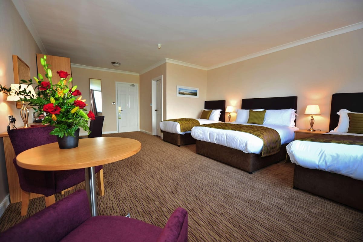 A hotel room with two beds, a dining table, a chair, and a potted plant.