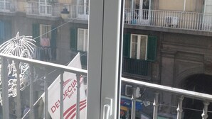 A view through a window with a metal railing, featuring a building with balconies and a street below. - Dei Decumani (Naples)