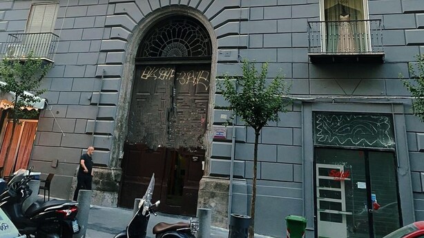 A multi-story building with a red facade, multiple balconies, and a large arched entrance. - Dei Decumani (Naples)