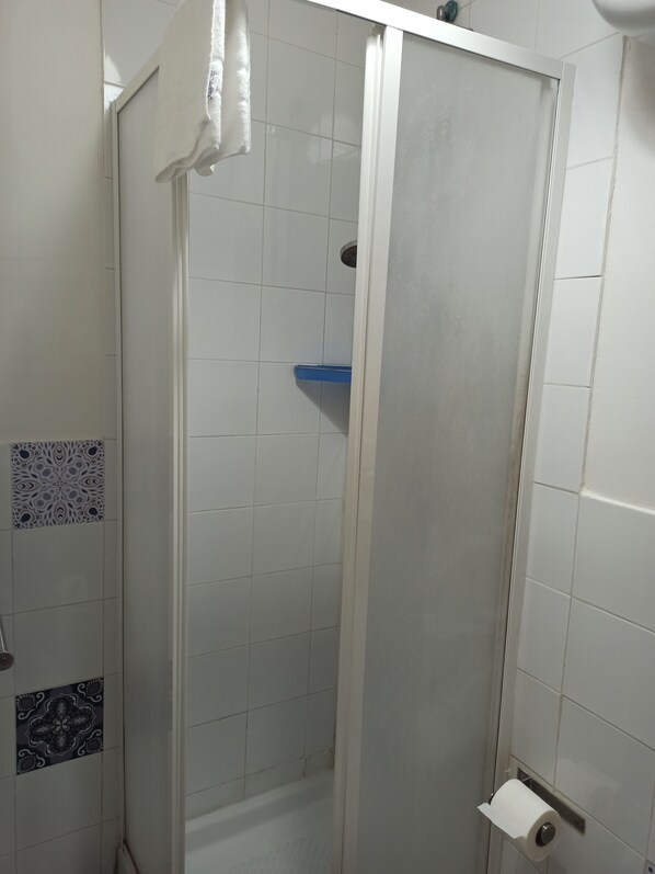 A shower area with a glass door, white tiled walls, and a blue shelf.