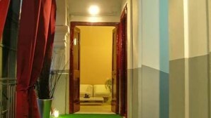 A hallway with a green carpet leading to a room with a bed and a nightstand. - Dei Decumani (Naples)