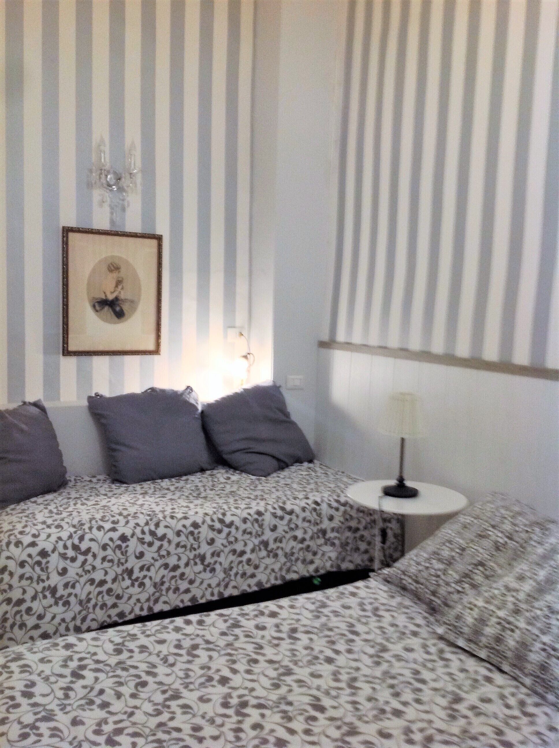 Habitación de hotel con dos camas, papel tapiz a rayas, un cuadro en la pared y una mesita de noche con lámpara.