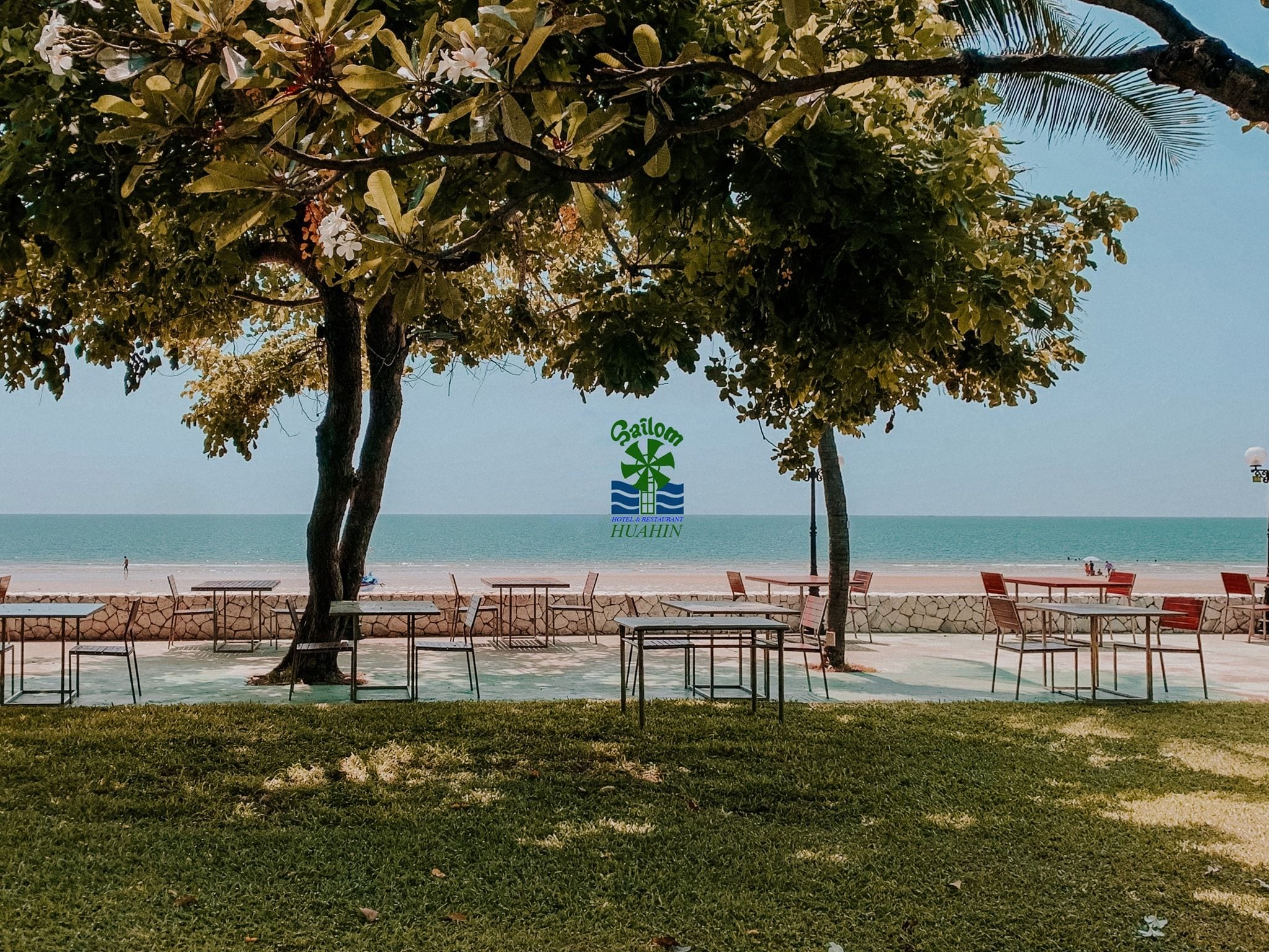 A beachside view with a hotel sign, outdoor seating, and a clear view of the ocean.