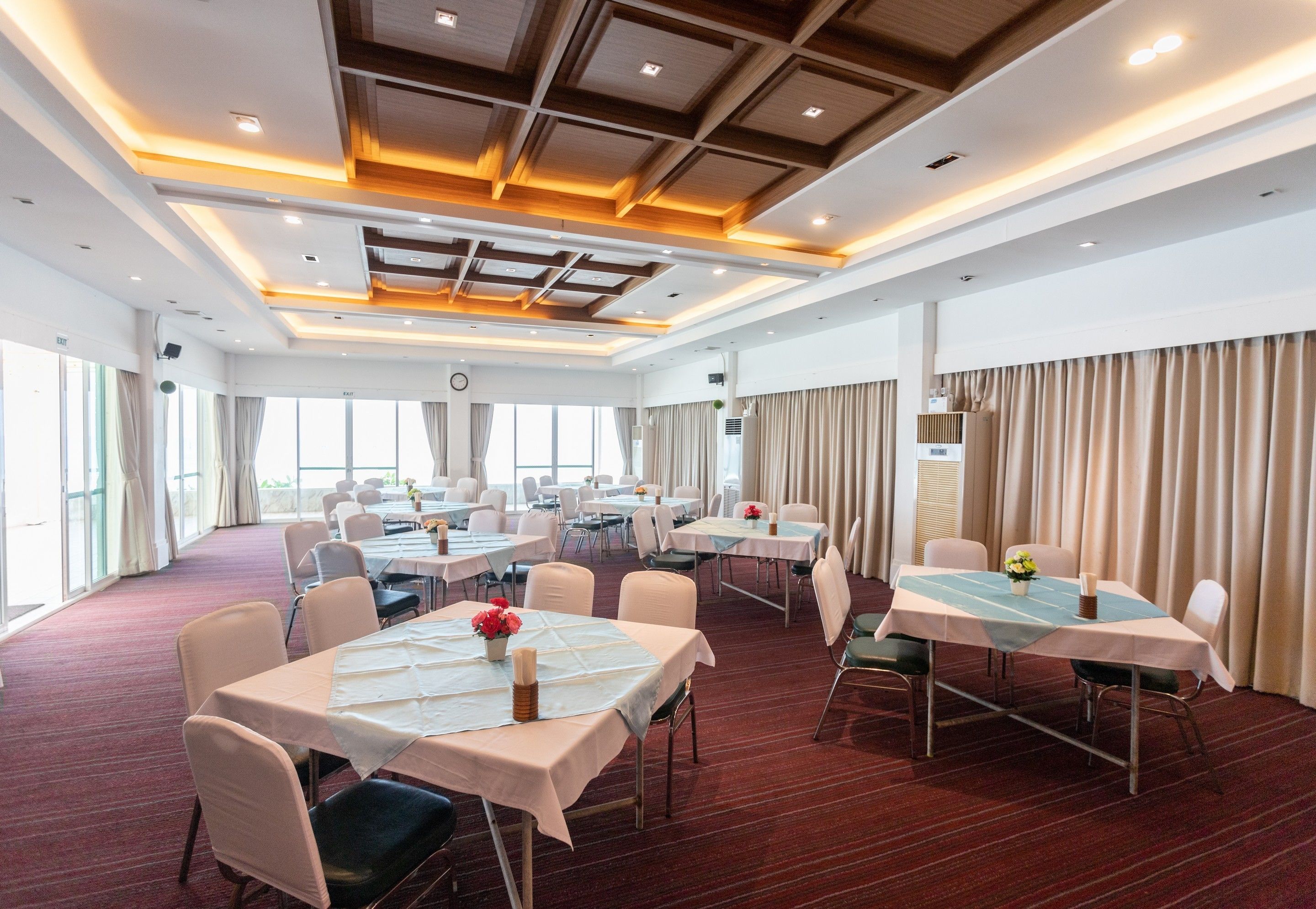 A large conference room with multiple tables and chairs, equipped with ceiling lights and a visible clock.