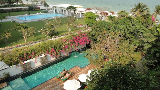A pool area with a view of the ocean, surrounded by lush greenery and a white building. - Sailom Hotel Hua Hin (Hua Hin)