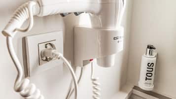 A hairdryer mounted on a wall, a plug, and a canister labeled 'TOUS' on a shelf.