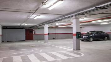 Un estacionamiento interior con líneas pintadas de blanco y rojo, pilares de hormigón e iluminación fluorescente.