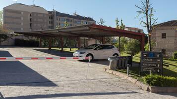 Ein Parkplatz mit einem weißen Auto, einem überdachten Gang und einem Schild, das die Wege zum Parkplatz, zur Rezeption und zur Cafeteria weist.