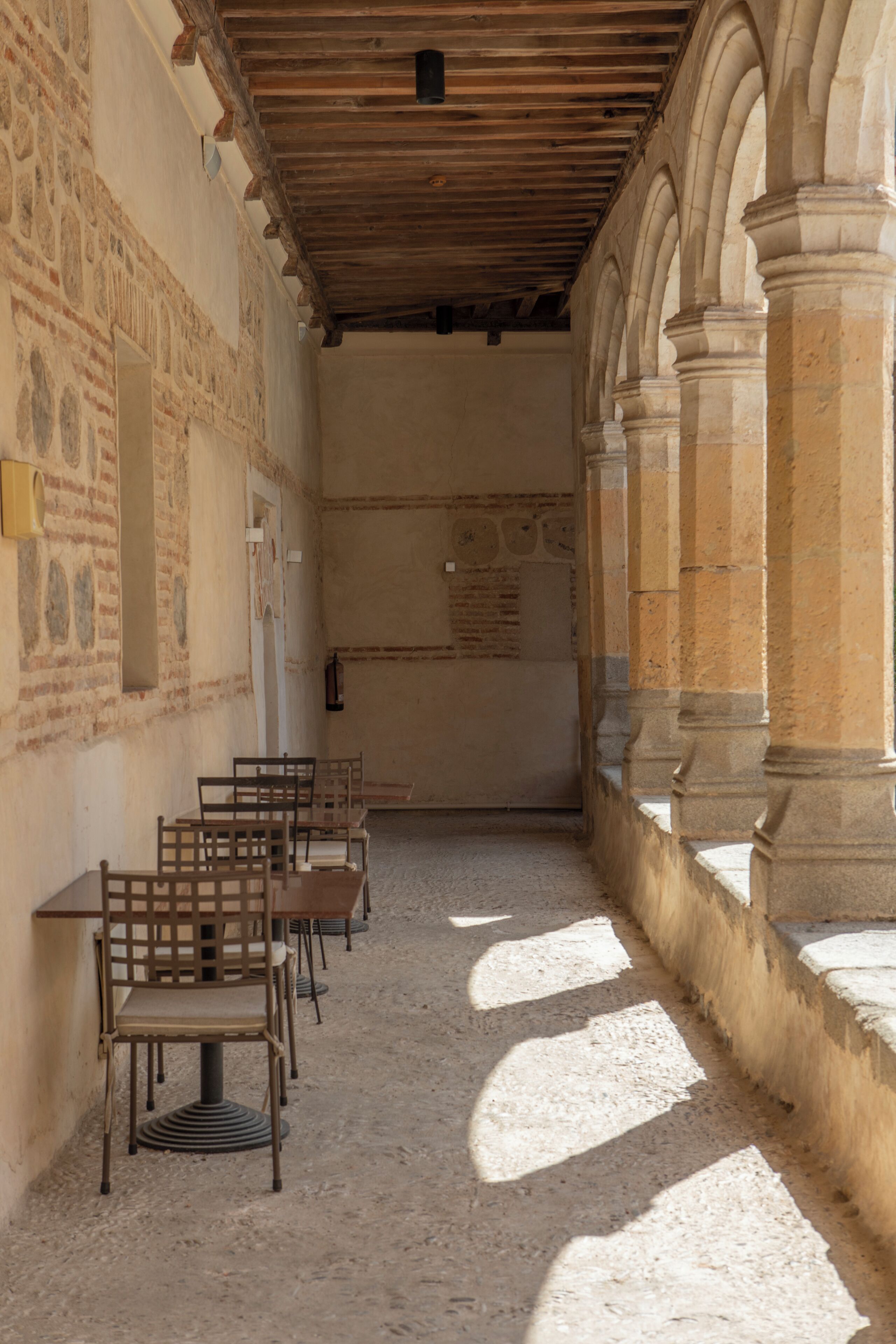 A corridor with stone walls, wooden benches, and a tiled floor.