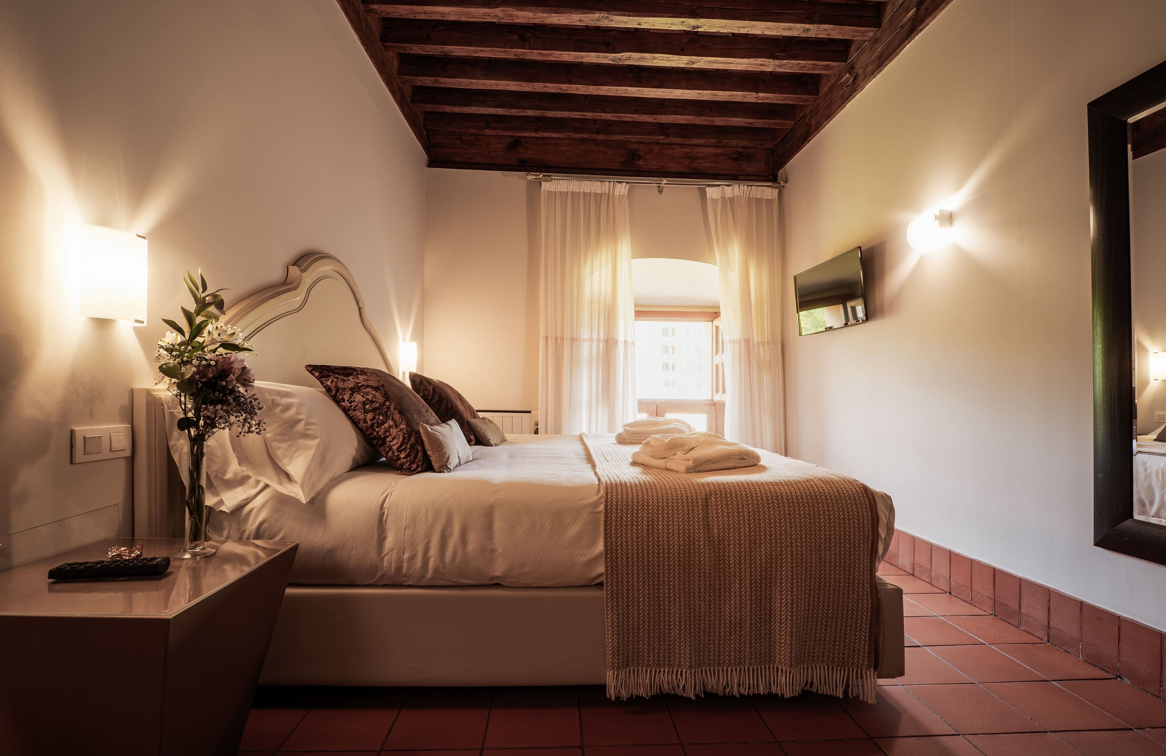 A bedroom with a bed, bedside table, lamp, and a mirror on the wall.