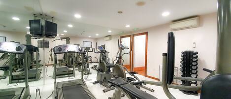 Un gimnasio con equipos de ejercicio variados, incluyendo cintas de correr, máquinas de pesas y una prensa de banca.