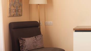 A room with a dark brown leather chair, a white desk, a wall-mounted lamp, and a colorful abstract painting.