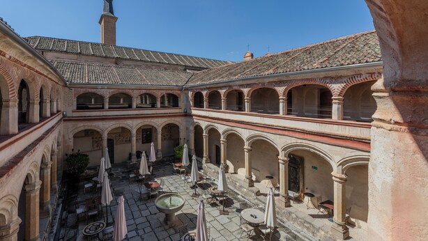 Un patio con varios niveles de arcos, zonas de estar al aire libre y la cúpula de una iglesia a la vista.