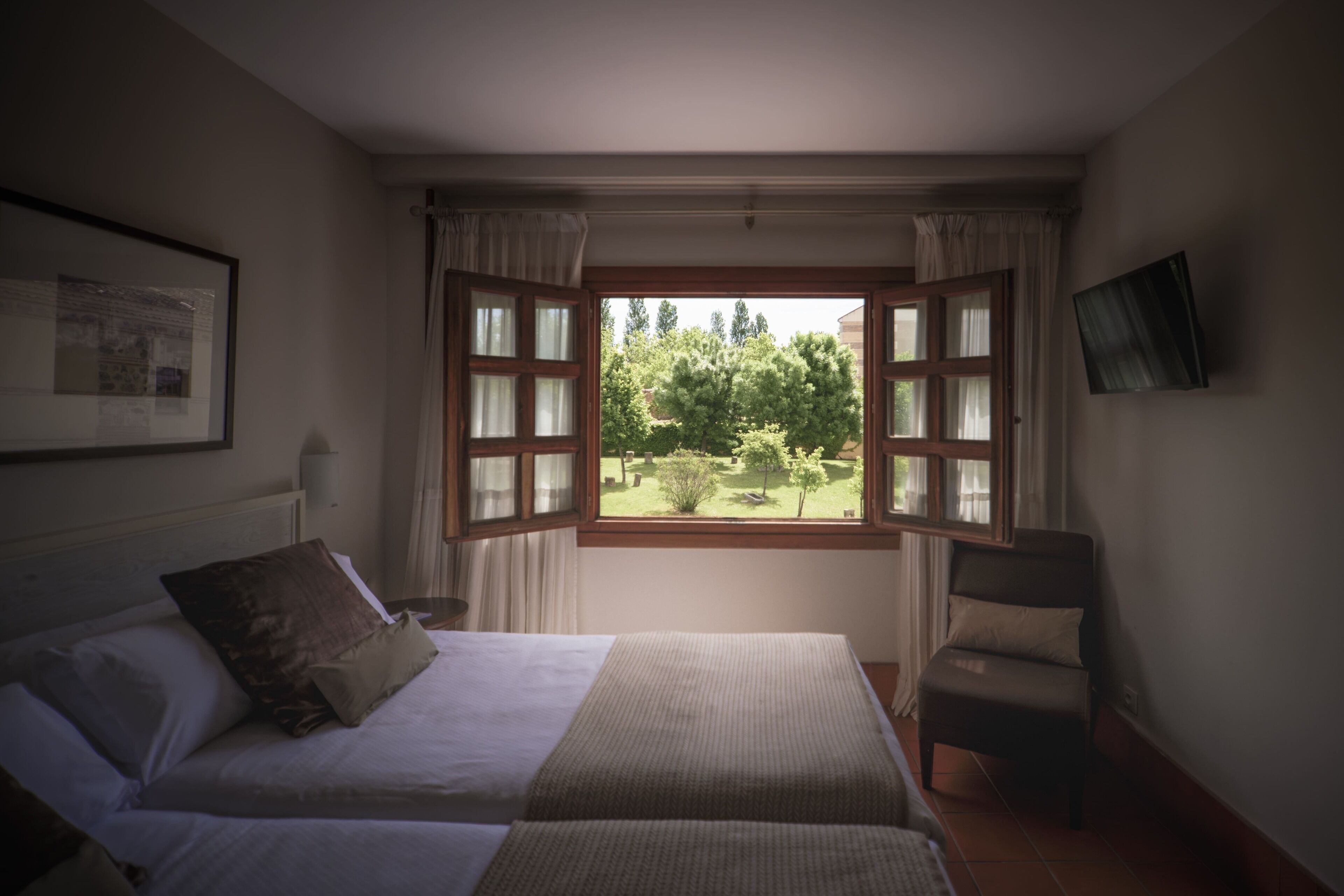 Une chambre avec une grande fenêtre, un lit, une chaise et un tableau encadré au mur.