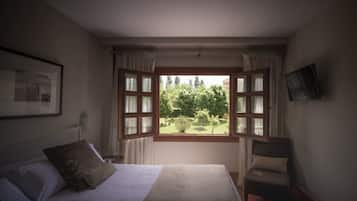 Une chambre avec une grande fenêtre, un lit, une chaise et un tableau encadré au mur.