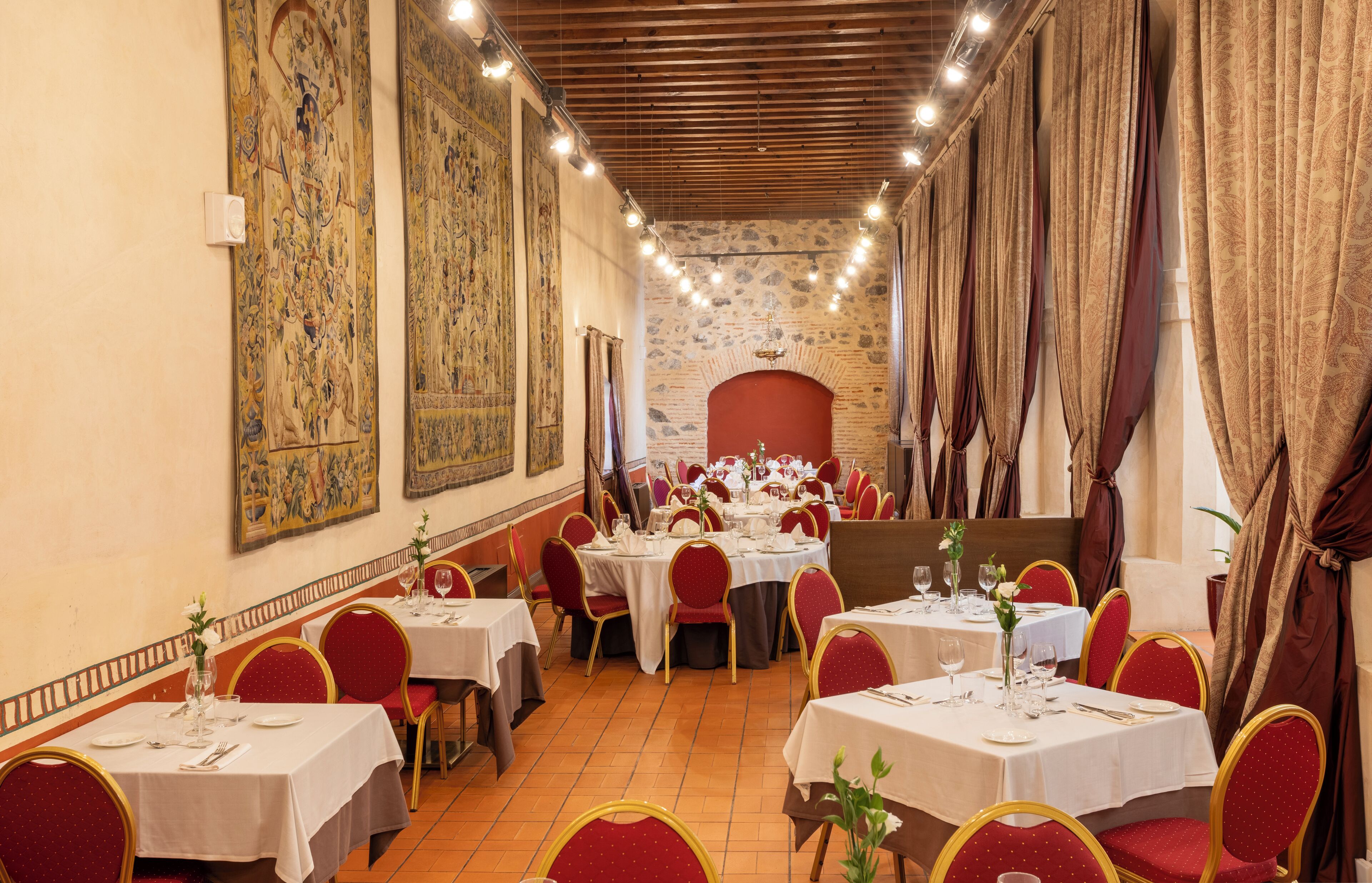 A restaurant with round tables, red chairs, and large tapestries on the walls.