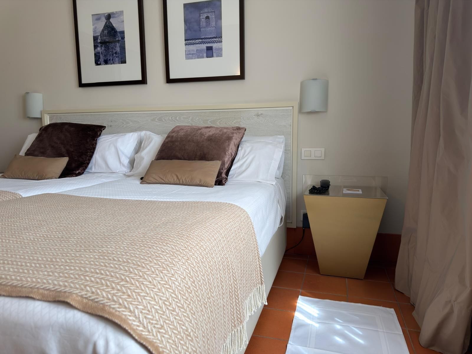 Een hotelkamer met een bed, twee ingelijste foto’s aan de muur, een nachtkastje en een gordijn.
