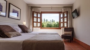Habitación de hotel con dos camas, un televisor montado en la pared y una ventana con cortinas.