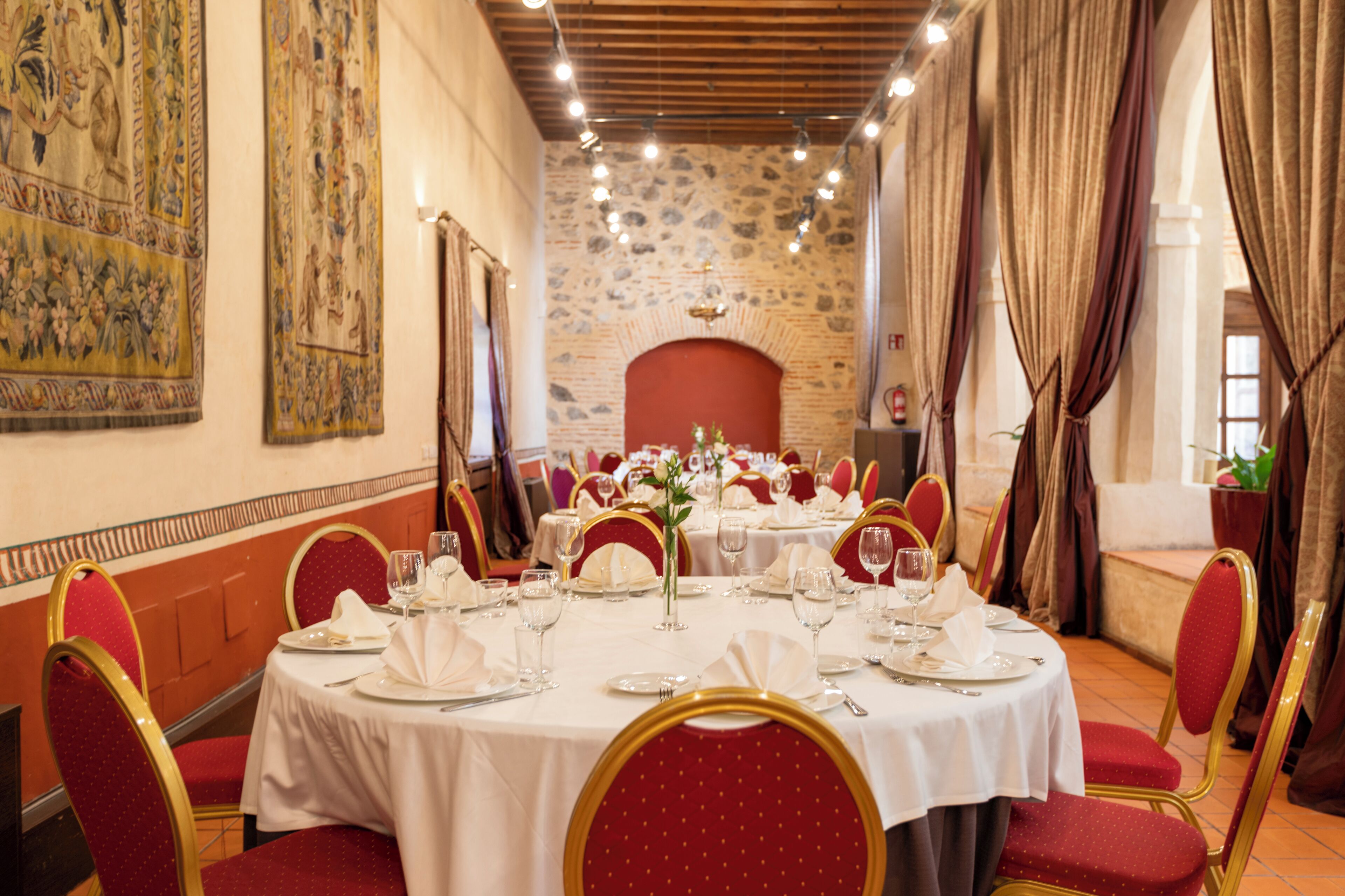 Un comedor formal con mesas redondas, sillas tapizadas en rojo y una pared de piedra con chimenea.