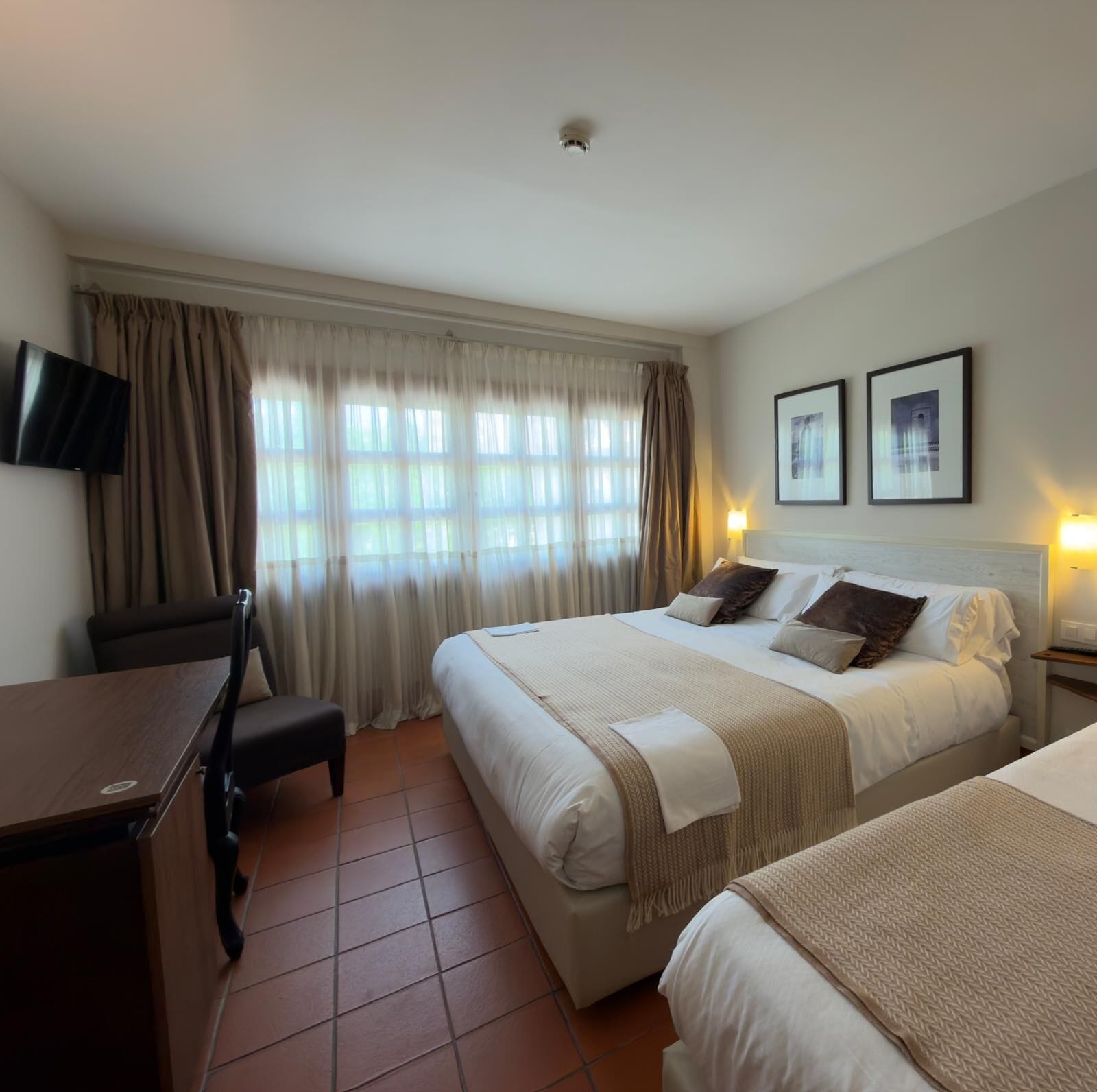 Ein Hotelzimmer mit einem Bett, Nachttischen, einem Schreibtisch, einem Stuhl und einem Fernseher.