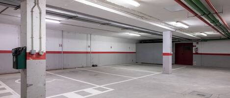 A clean, empty parking garage with white walls, red and white lines marking parking spaces, and fluorescent lighting.