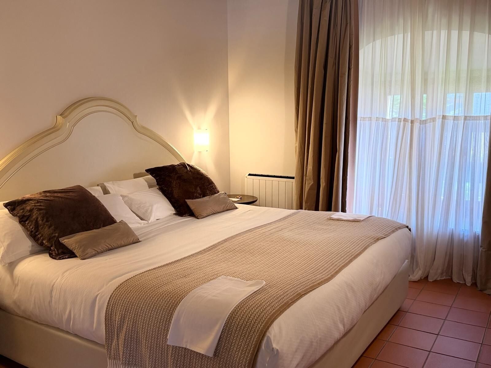 A neatly made bed with a headboard, pillows, a bedside table, and a lamp.