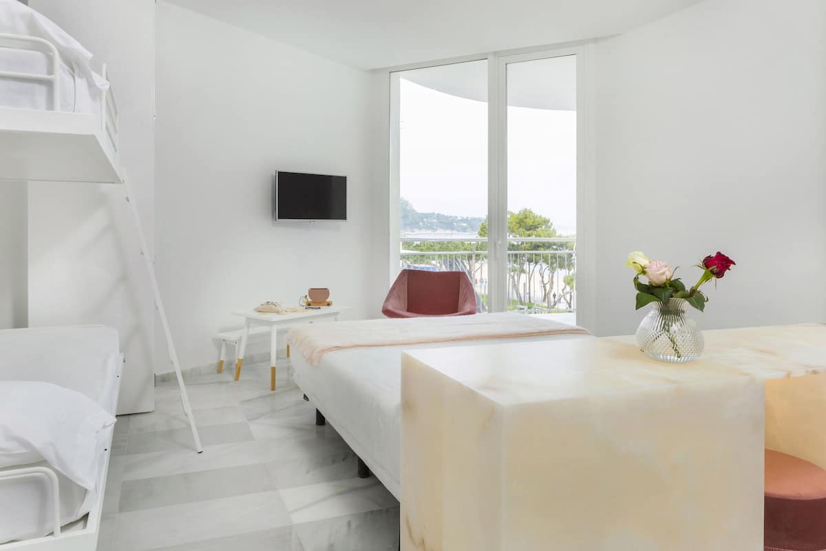 Ein Hotelzimmer mit Etagenbett, Schreibtisch, Stuhl, Fernseher und einem Balkon mit Aussicht.