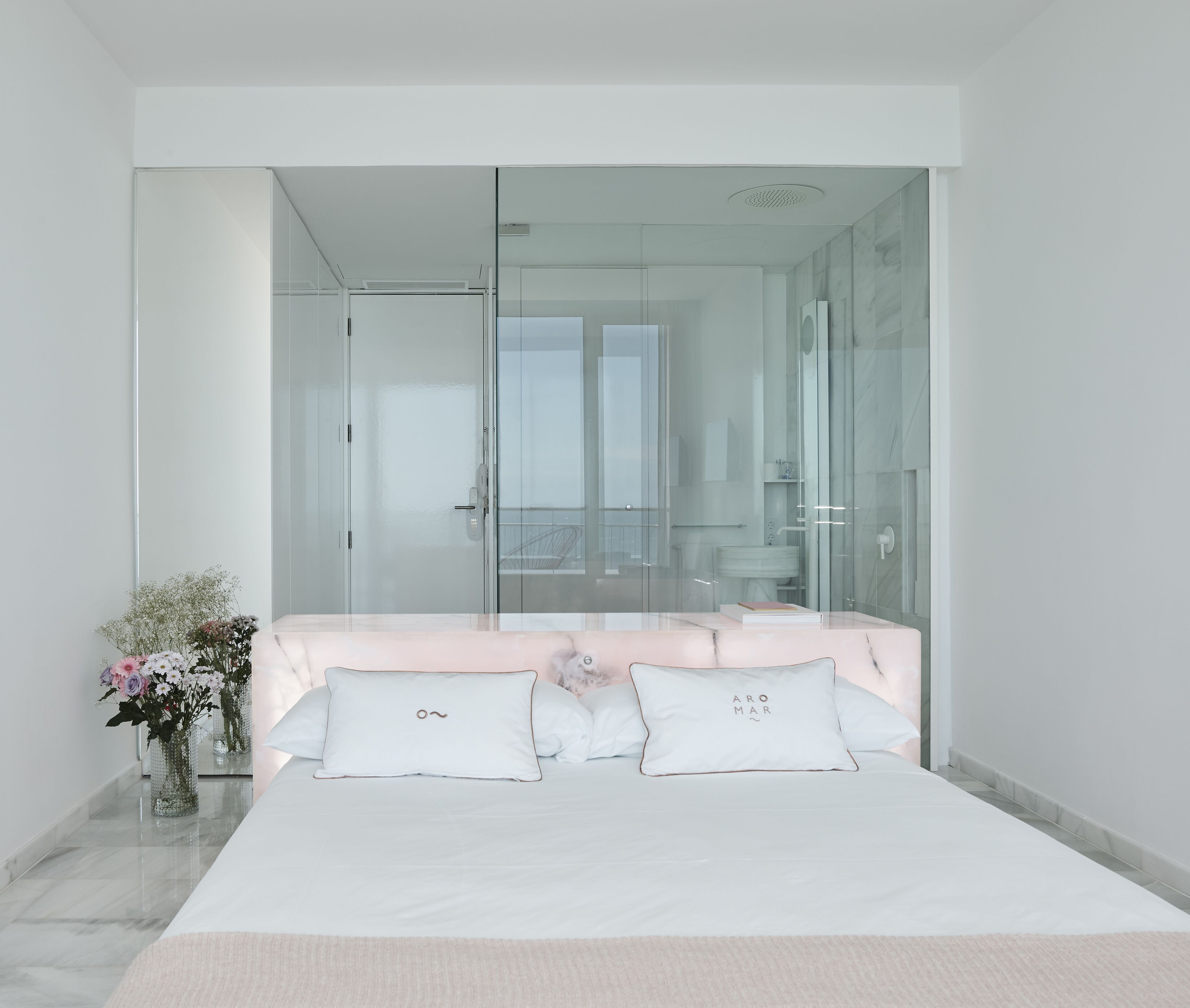 Een slaapkamer met een bed, een nachtkastje, een vaas met bloemen en een glazen kledingkast.