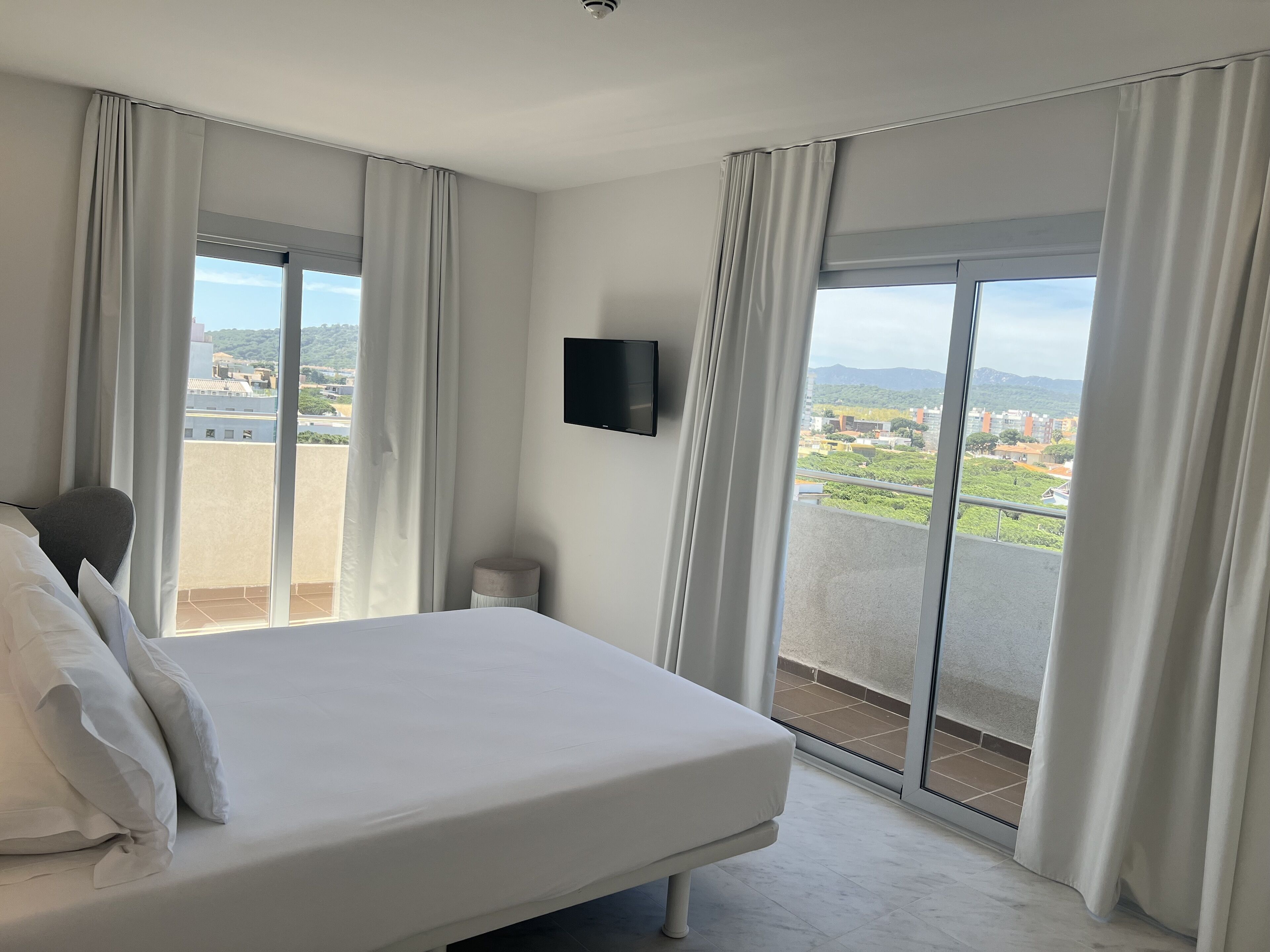 Une chambre d’hôtel dotée d’un grand lit, d’un téléviseur à écran plat fixé au mur et d’un balcon offrant une vue sur la ville.