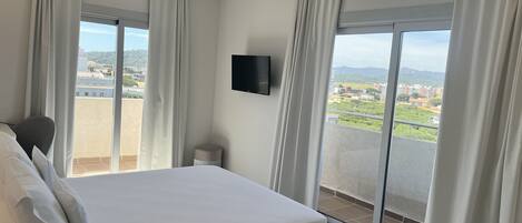 Une chambre d’hôtel dotée d’un grand lit, d’un téléviseur à écran plat fixé au mur et d’un balcon offrant une vue sur la ville.