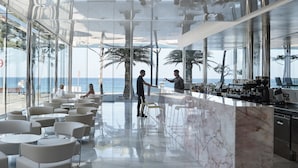 Un bar moderno con mostrador de mármol, asientos de estructura metálica y grandes ventanales con vistas al mar.