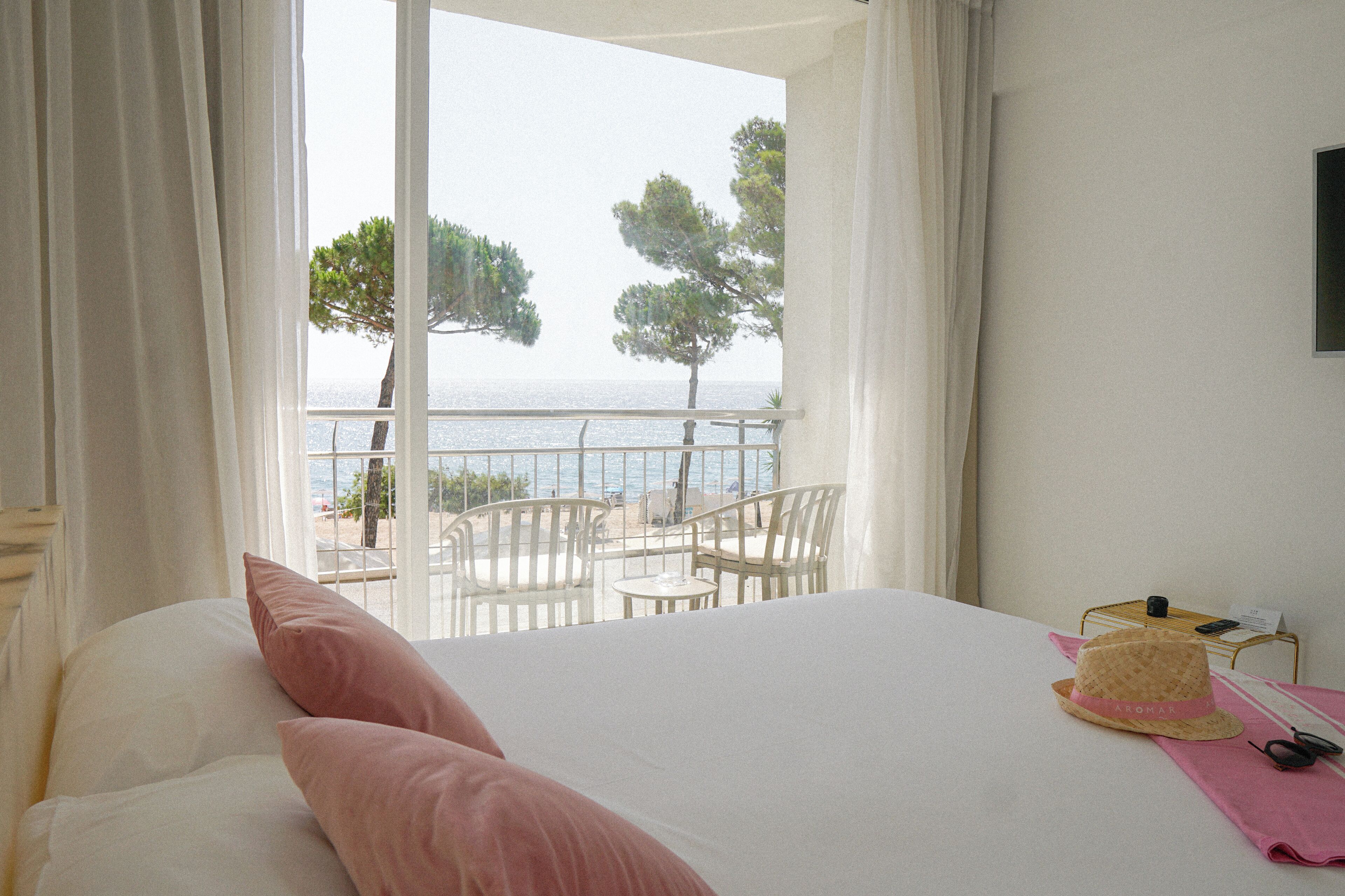Une chambre d’hôtel avec un lit, un balcon avec des chaises et une vue sur la mer et les arbres.
