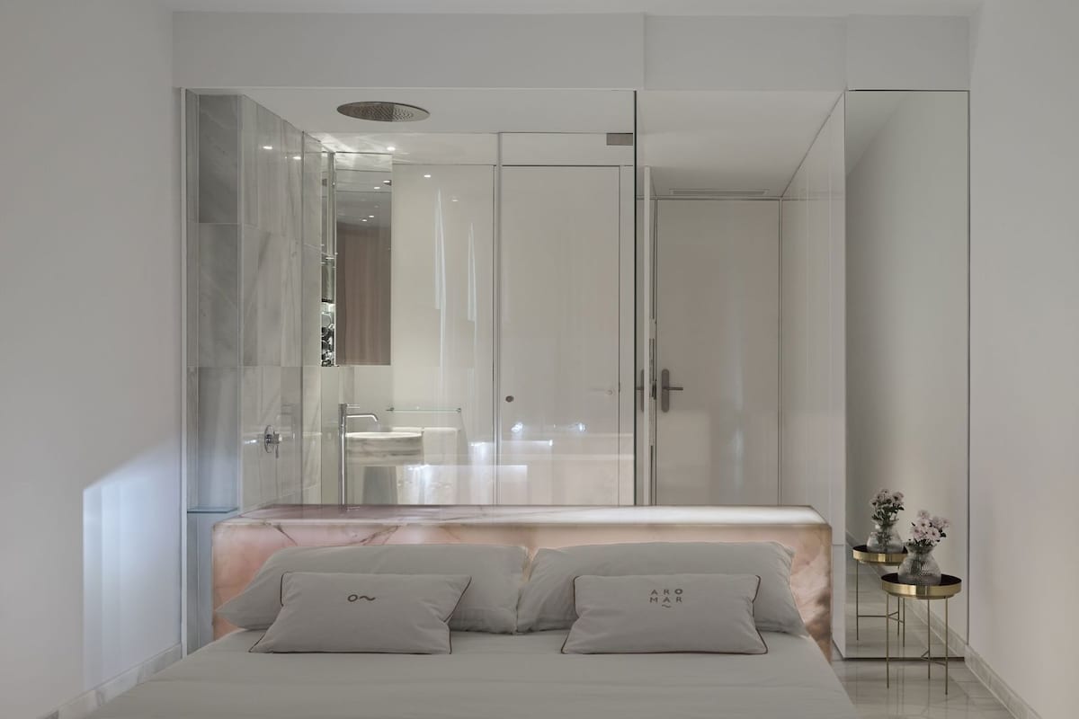 Un dormitorio moderno con una cama, cabina de ducha de vidrio y una mesita de noche con un florero.