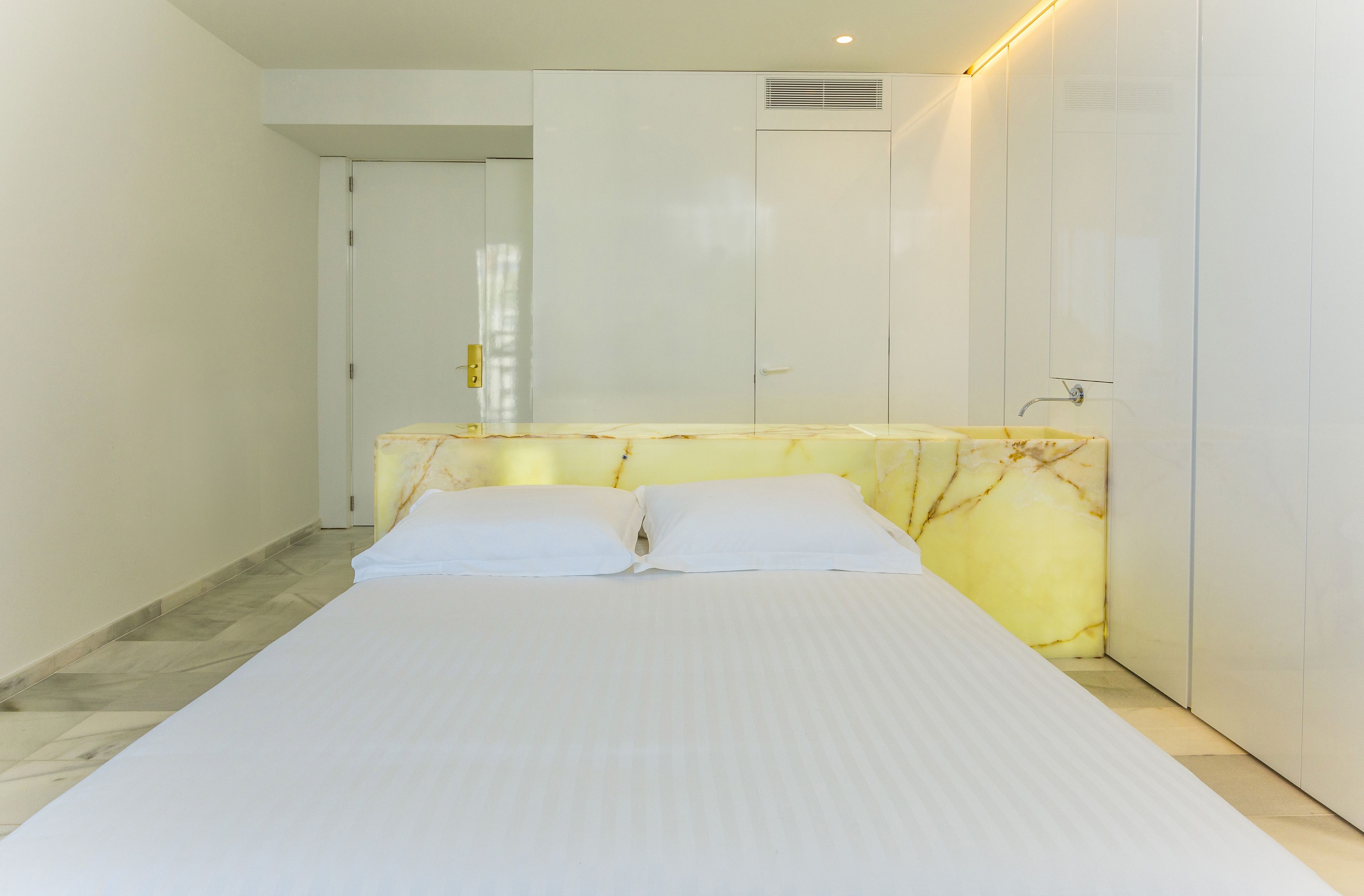 A bedroom with a bed, a marble headboard, a white door, and a white wardrobe.
