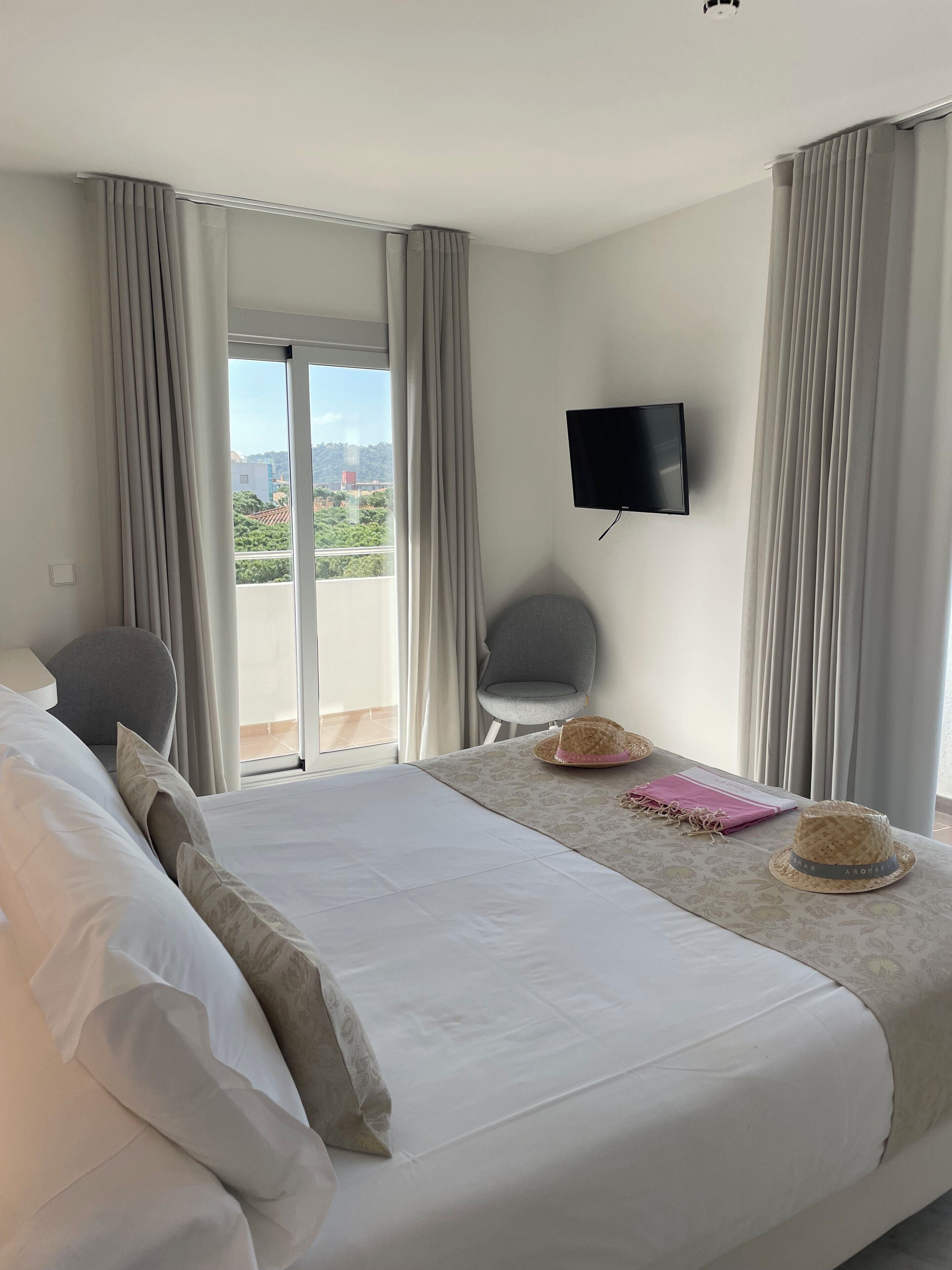 Quarto de hotel com uma cama grande, TV fixada na parede e vista para a cidade pela janela.
