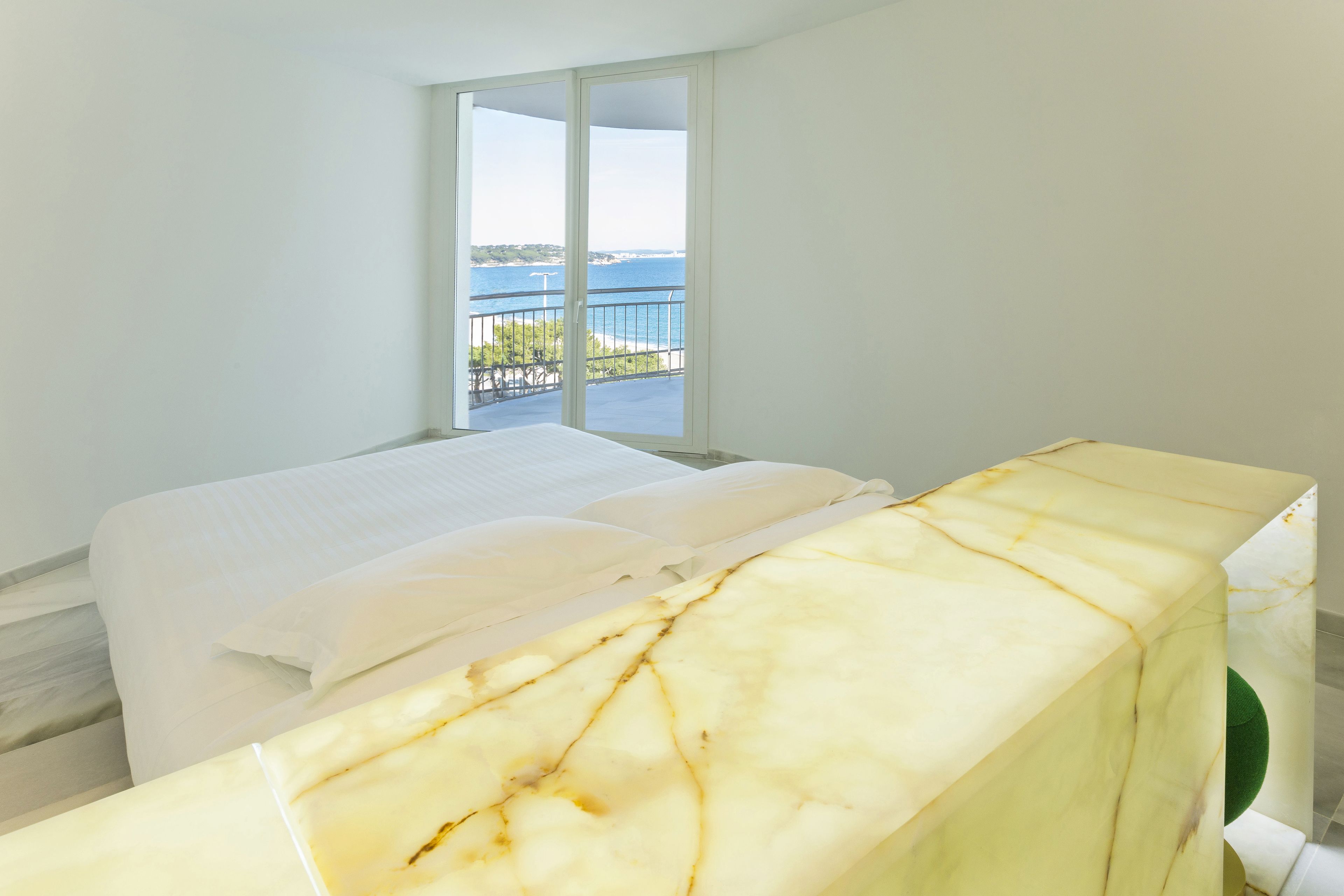 Una camera da letto con un letto, un comodino in marmo e un balcone vista mare.