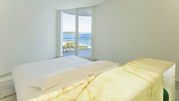 Una camera da letto con un letto, un comodino in marmo e un balcone vista mare.